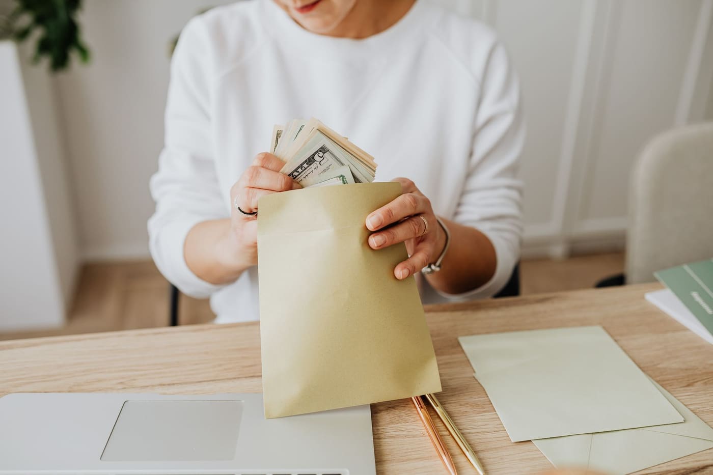 A person putting cash into paper envelopes at a wooden desk