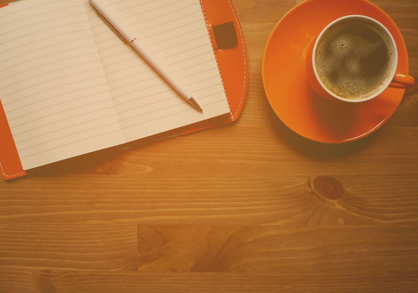 A cup of coffee beside an open lined notebook with a pencil on a wooden table
