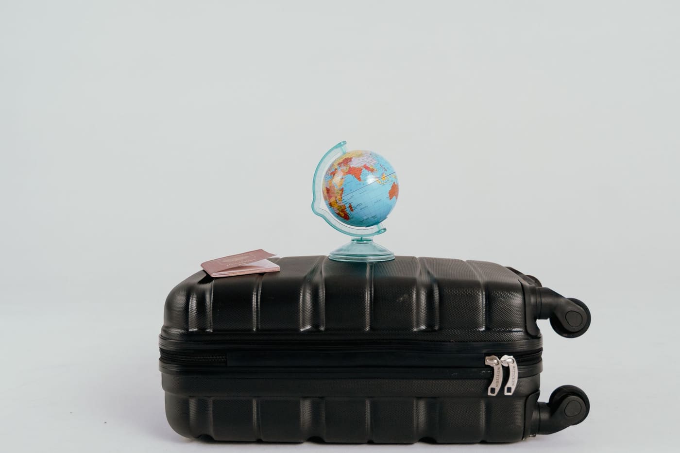 A small globe and a passport resting on top of a black rolling suitcase