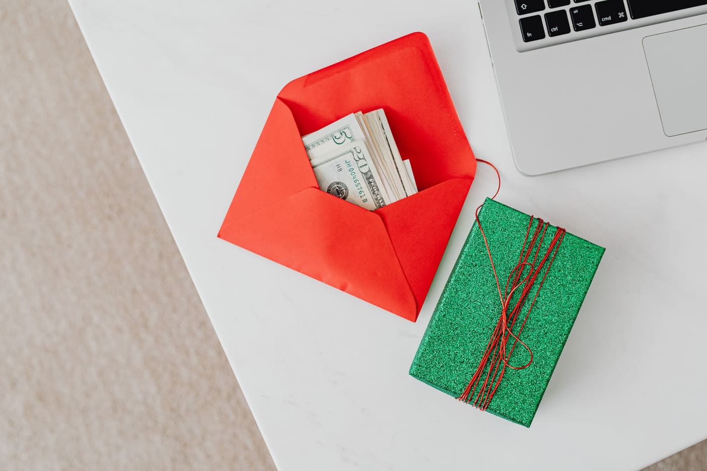 A green wrapped gift box beside a red envelope holding cash on a white desk