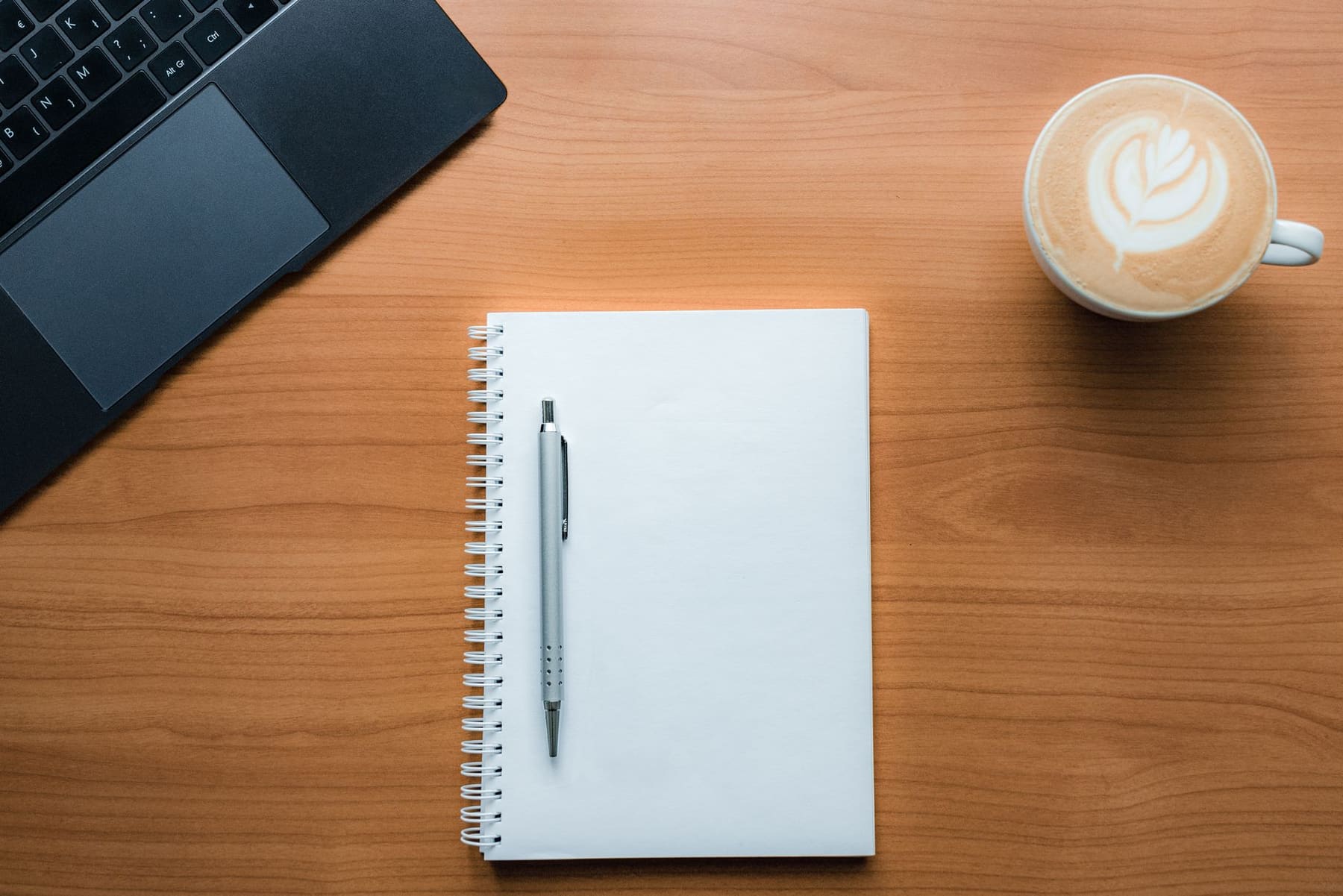 A notebook, pen and coffee cup on a bright wooden desk