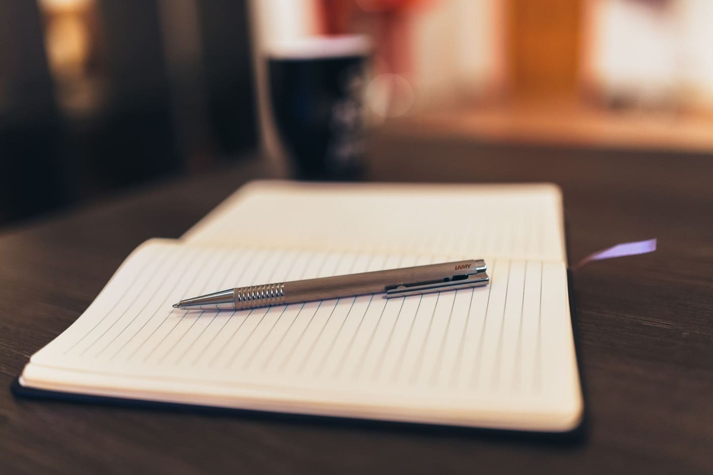 An open notebook with a pen lying on it and a mug in the background
