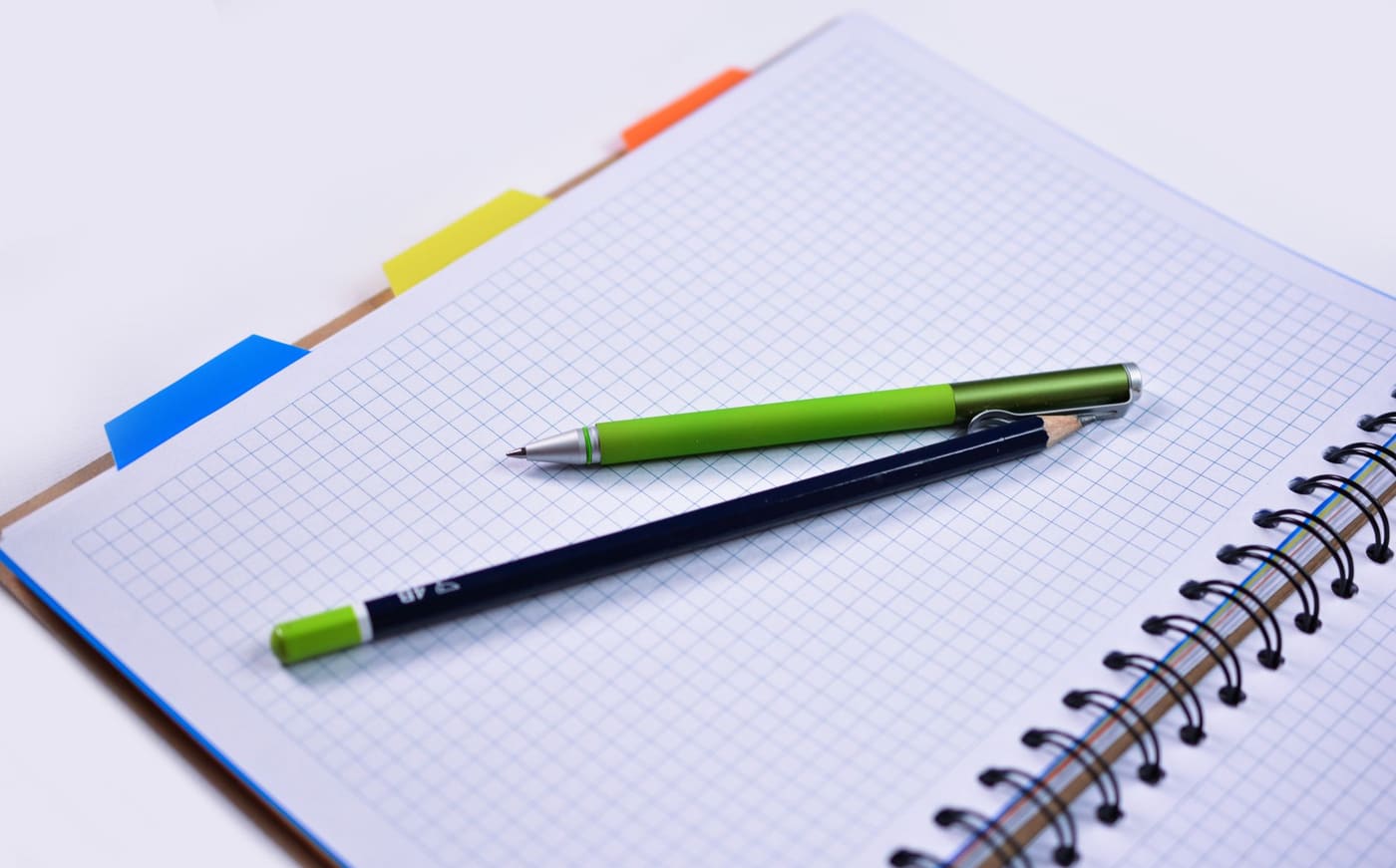 A spiral notebook with graph paper and two pens