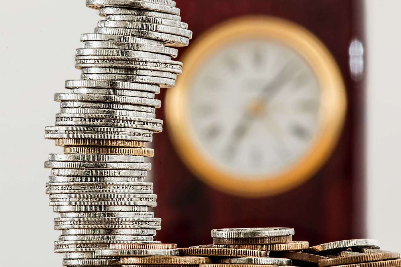 Stacks of coins in front of a blurred clock