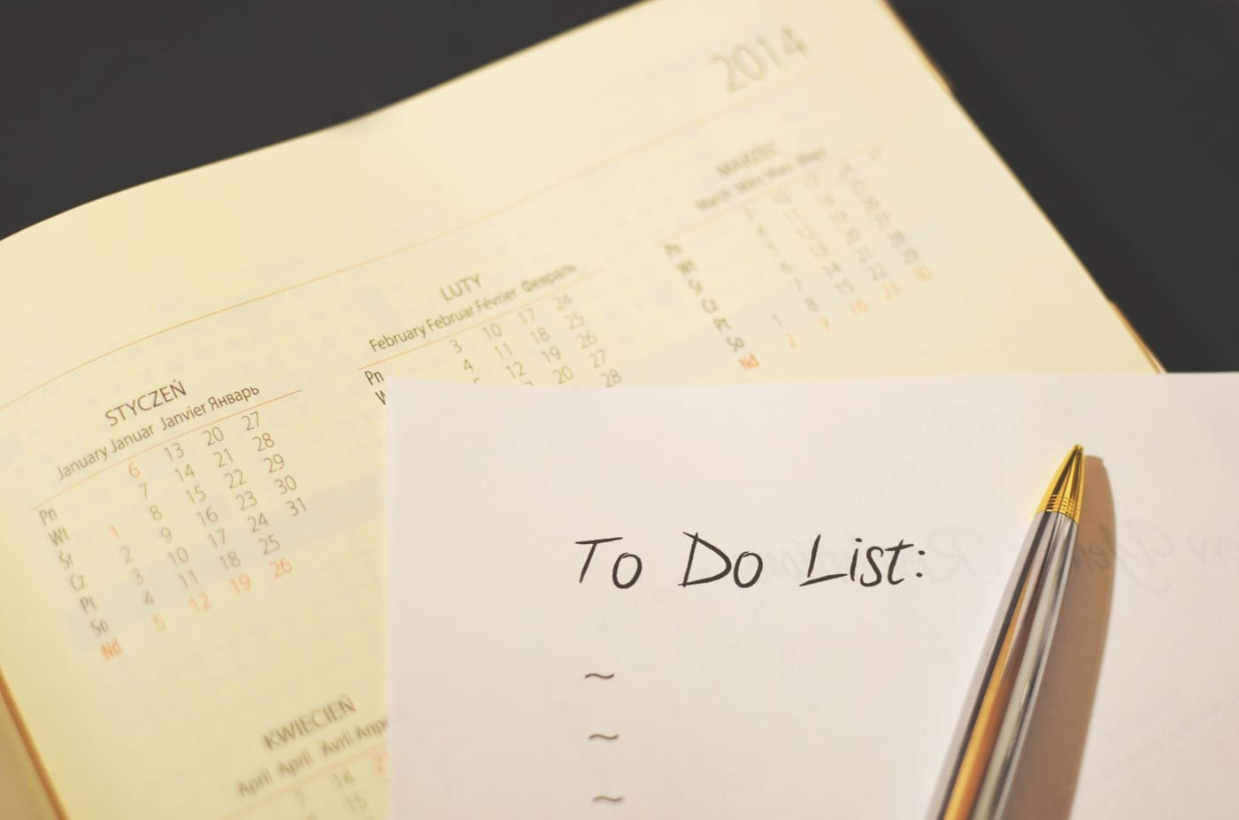 A handwritten to-do list on paper beside a calendar page and a pen