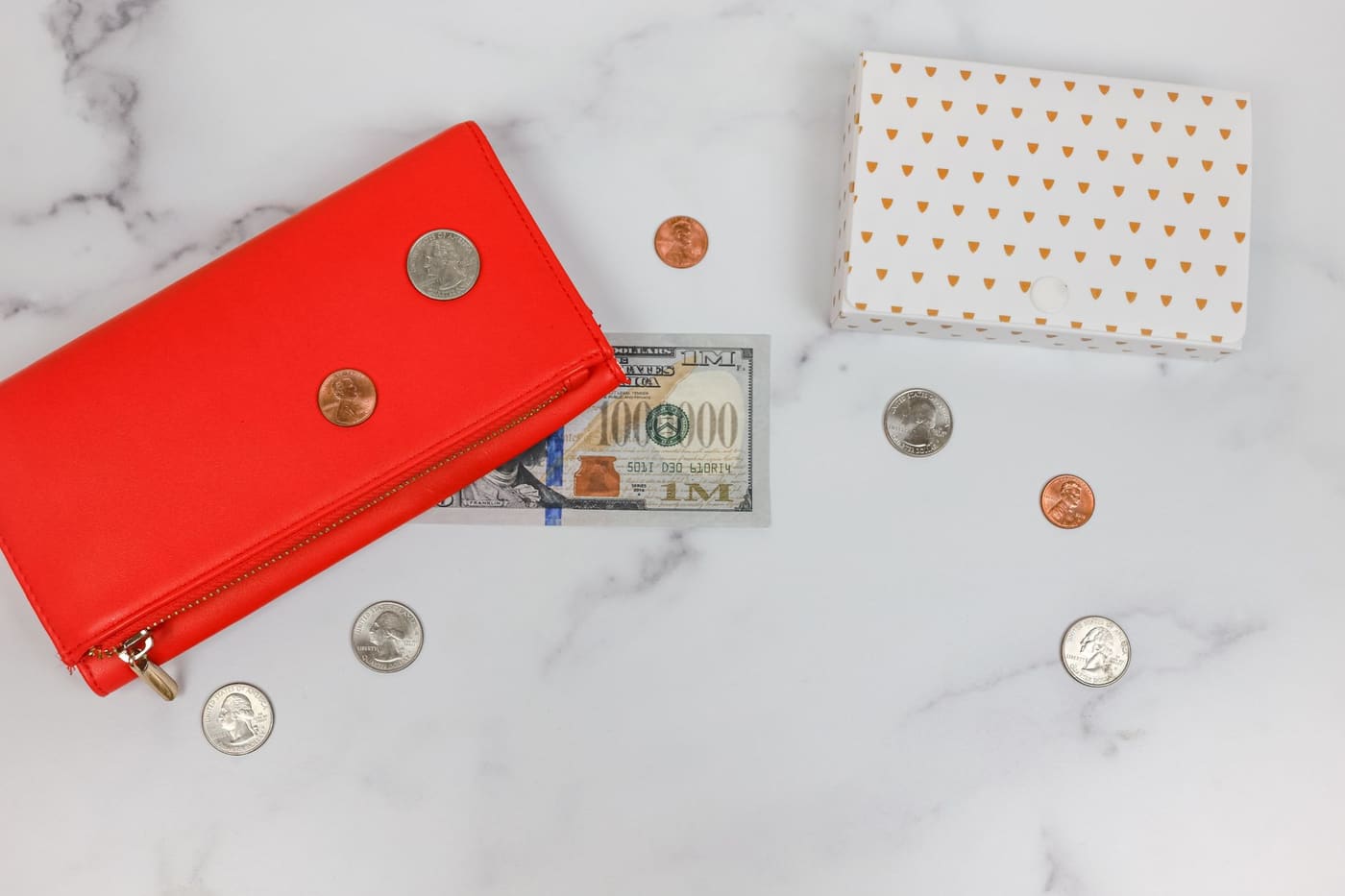 A red wallet with a dollar bill and coins scattered on a marble surface